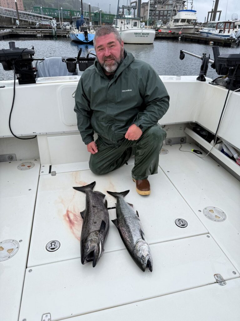 Captain Cable kneeling on the back deck of the 4 C's vessel at the dock with two freshly caught king salmon.